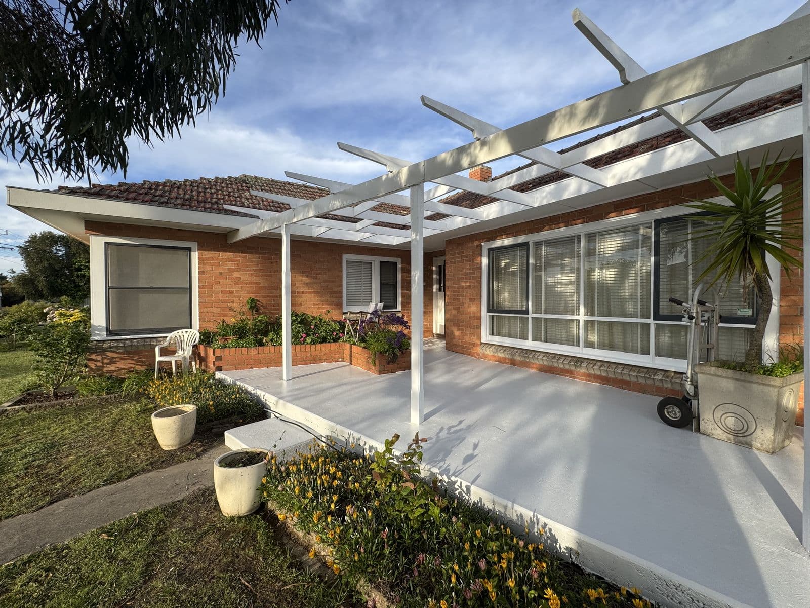 Red-brick home with a white pergola and white window trim